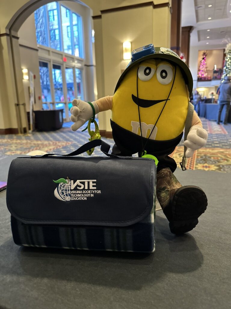 The signature VSTE M&M mascot standing behind a VSTE blanket.
